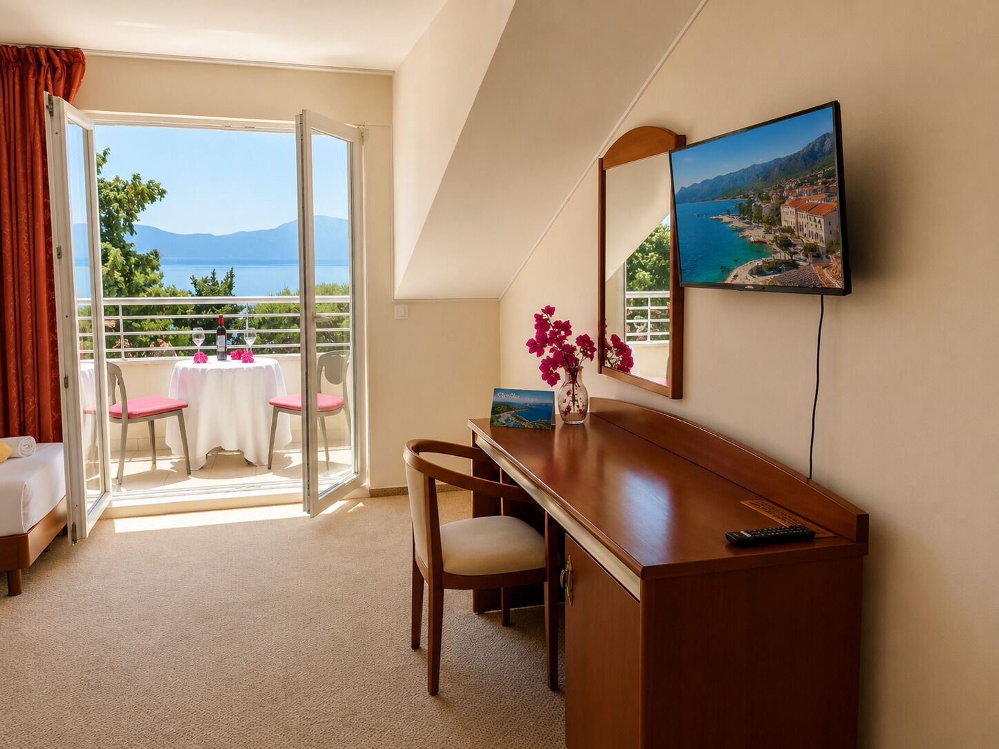 A hotel room with a balcony, a desk, a chair, a bed, a TV, and a painting.
