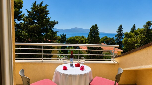 Un balcón con una mesa lista para dos personas, con vistas panorámicas al mar y las montañas.