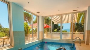 Una piscina interior con paredes de vidrio transparente, suelo de baldosas y una escalera de piscina.