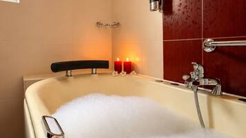 A bathtub filled with bubbles, a handheld showerhead, and two lit candles on the wall.