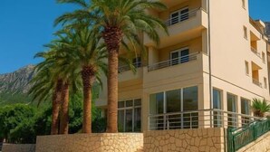Un edificio de varios pisos con balcones, fachada de piedra y palmeras.