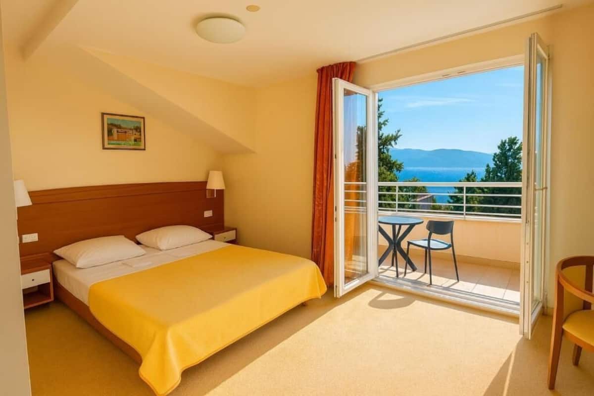 A hotel room with a bed, a nightstand, a table with chairs, and a balcony with a view.