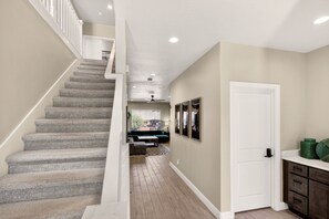 A staircase leading to a living area with a sofa and a coffee table, a white door, and a wooden floor. - 5BR Utah Escape Near Zion – Pool and Grill (Hurricane)