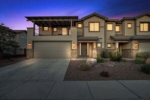A modern two-story house with a garage, stone accents, and a well-lit driveway. - 5BR Utah Escape Near Zion – Pool and Grill (Hurricane)