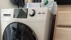 Etukuormauspyykinpesukone, jossa on ohjauspaneeli ja puinen kotelo, ja taustalla näkyy polkupyörä.