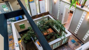 Un intérieur à plusieurs niveaux, doté d’un atrium central comprenant un escalier, un petit coin salon et diverses plantes.