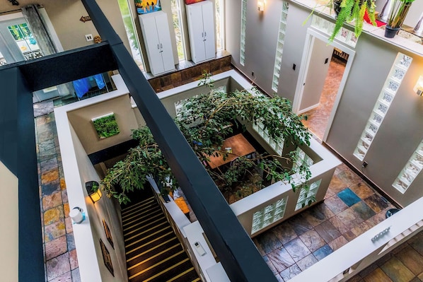 Een meerlaags interieur met een centraal atrium, voorzien van een trap, een klein zitgedeelte en diverse planten.