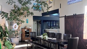Un vaste espace à manger avec un haut plafond, un grand arbre et une vue sur la cuisine.