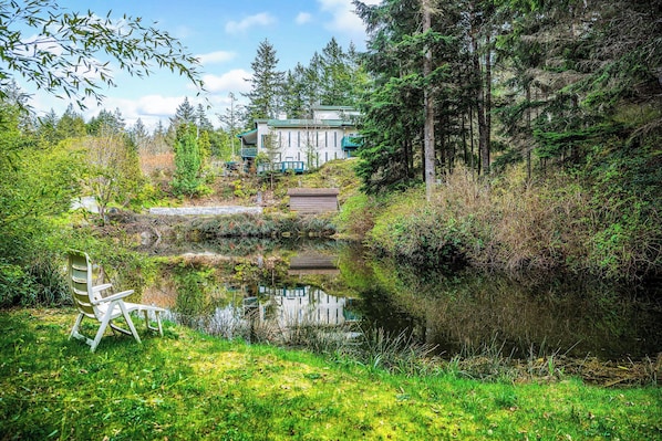 A house with a deck, surrounded by dense forest and a pond. - Koi Pond & Meditation Gardens Await In The Quiet Rainforest of East Sooke (Sooke)
