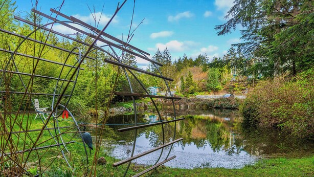 Un étang paisible, agrémenté d’une structure métallique, et entouré d’une végétation luxuriante et d’arbres.