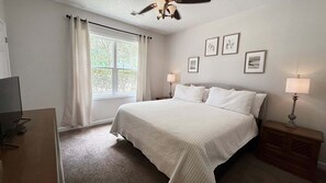 Ein Schlafzimmer mit einem Bett, zwei Nachttischlampen, einem Fenster mit Vorhängen und drei gerahmten Bildern an der Wand.
