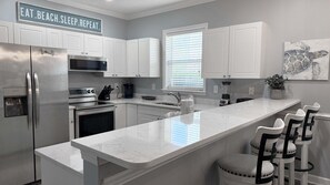Eine moderne Küche mit weißen Schränken, einem Edelstahlkühlschrank, einem eingebauten Backofen, einer Mikrowelle und einer großen Kücheninsel mit Barhockern.