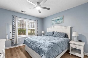 Ein Schlafzimmer mit einem Bett, Nachttischen, einem Deckenventilator, einem Fenster mit Vorhängen und einem Bild an der Wand.