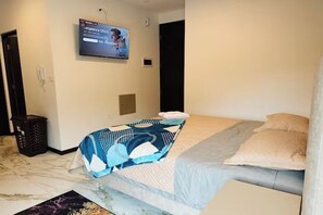 Ein Hotelzimmer mit einem Bett, einem an der Wand montierten Fernseher, einer Mülleimer und einer Tür.