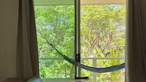 Une pièce comprenant un bureau, une chaise et offrant une vue sur la verdure grâce à une grande fenêtre.
