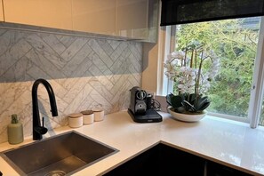 Une cuisine moderne avec un dosseret en marbre, un robinet noir, une machine à café et une orchidée en pot près d’une fenêtre.