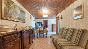 Ein Zimmer mit Holzboden, einer Couch, einem Esstisch mit Stühlen, einer Küchenzeile und einem großen gerahmten Gemälde.