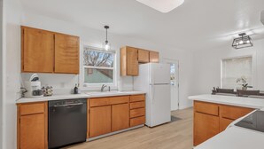 A modern kitchen with wooden cabinets, a dishwasher, a refrigerator, and a window with a view.