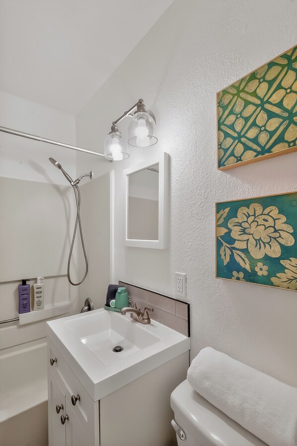 Une salle de bain avec un lavabo blanc, un miroir, une pomme de douche et une serviette.