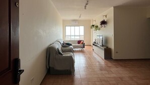 En rummelig opholdsstue med sofa, fjernsyn og et vindue der lukker naturligt lys ind.