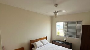 Et soveværelse med en seng, en enkeltseng, et natbord, en lampe, en ventilator i loftet og et vindue med persienner samt udsigt til det fri.