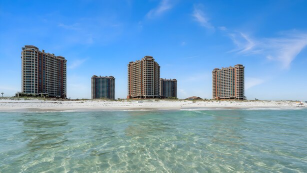 Ein Strandhotel mit mehreren Hochhäusern, klarem türkisblauem Wasser und einem Sandstrand.