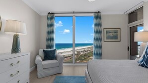 Ein Schlafzimmer mit großem Fenster, einem Bett, einem Sessel, einem Schminktisch und einem Gemälde.