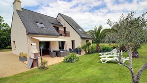 Una casa de dos pisos con un patio, mobiliario exterior y un jardín.