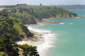 Paisagem costeira com praia, falésias e um farol ao longe.