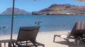 Une plage avec des chaises longues et des parasols, une île rocheuse en arrière-plan et un ciel bleu dégagé.