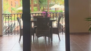 Un balcon avec une table et des chaises pour prendre les repas, une vue sur des palmiers et un bâtiment en arrière-plan.