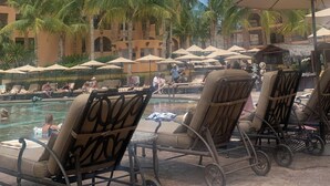 Un espace aménagé au bord de la piscine, avec des chaises longues, des parasols et, au fond, un bâtiment doté d’un toit rouge.