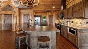 Una cucina rustica con pareti in legno, un'isola centrale, sgabelli da bar e un lampadario.