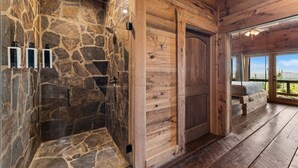 Una doccia in pietra con pareti in legno, una panca di legno e vista attraverso una grande finestra.