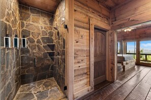 Eine Steindusche mit Holzwänden, einer Holzbank und Blick durch ein großes Fenster.