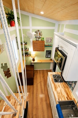A kitchen with a wooden countertop, a gas stove, a sink, a ceiling fan, and a window with rope curtains. - Cozy Tiny RV Stay Near Disneyland, LA & Orange County (Rowland Heights)
