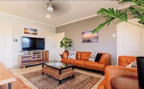 Ein Wohnzimmer mit Fernseher, Ledersofa, Couchtisch und einer großen Pflanze.