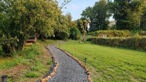 Ein Kiesweg, der von Felsen gesäumt und durch eine grüne Fläche mit Bäumen und einer kleinen Struktur führt.