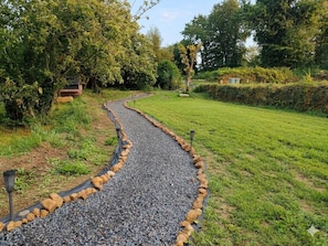 Ein Kiesweg, der von Felsen gesäumt und durch eine grüne Fläche mit Bäumen und einer kleinen Struktur führt.