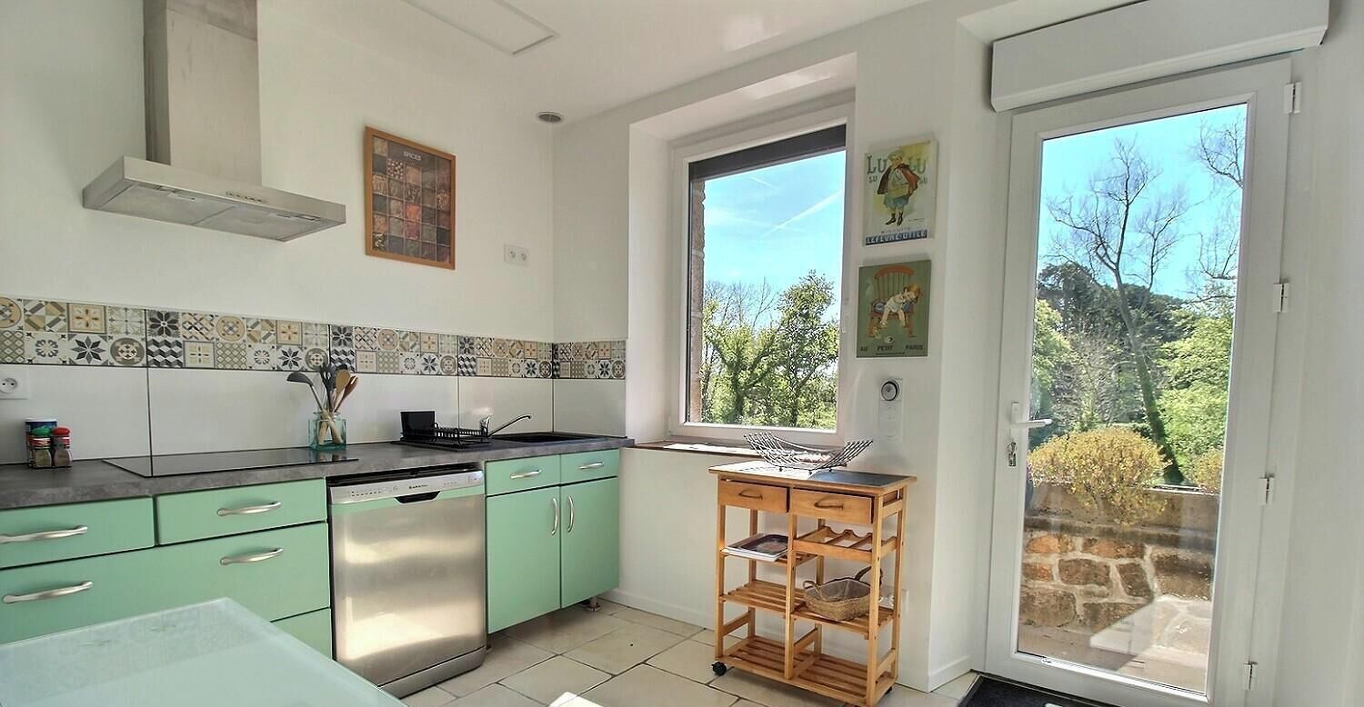 A kitchen with a dishwasher, green cabinets, a tiled backsplash, and a window with a view of trees.