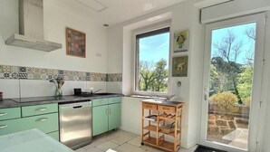 Eine Küche mit Geschirrspüler, grünen Schränken, einer gefliesten Spritzschutzwand und einem Fenster mit Blick auf Bäume.