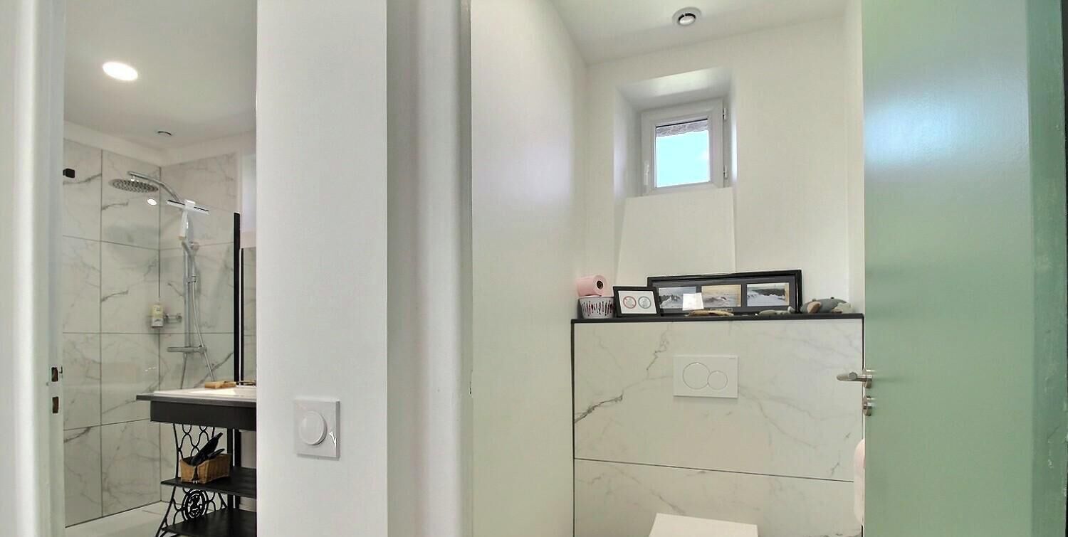 A bathroom with a shower, a small window, and a vanity with a mirror.