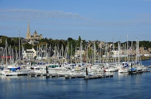 Ein Yachthafen mit zahlreichen Schiffen, eine markante Kirche mit hohem Turm im Hintergrund und eine Mischung aus Wohn- und Geschäftshäusern entlang der Uferpromenade.