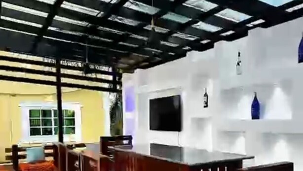 Una terrazza esterna con tavolo e sedie in legno, una TV montata su una parete bianca e un pavimento decorato.