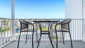 Un balcone con due sedie in vimini e un tavolo, con vista su un parcheggio e degli edifici.