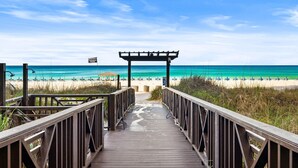 Passerella de fusta que condueix a una platja, amb una pèrgola i una bandera.