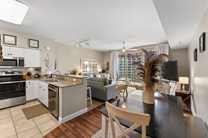Eine moderne Küche mit Kochinsel, ein Essbereich mit Tisch und Stühlen, eine Couch und ein großes Fenster mit Vorhängen.