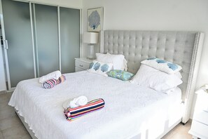 A neatly made bed with white bedding and colorful pillows, a bedside table with a lamp, and a wardrobe with frosted glass doors. - Modern 2-Bedroom Apartment in Bibijagua | Enjoy the Beach Just Steps Away (Playa Bibijagua)