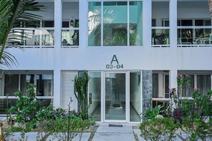 A modern building with a large glass door entrance, a balcony with plants, and a sign with the number 03-04. - Modern 2-Bedroom Apartment in Bibijagua | Enjoy the Beach Just Steps Away (Playa Bibijagua)