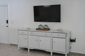 A white cabinet with drawers, a flat-screen TV mounted on the wall, and a power outlet on the wall. - Modern 2-Bedroom Apartment in Bibijagua | Enjoy the Beach Just Steps Away (Playa Bibijagua)